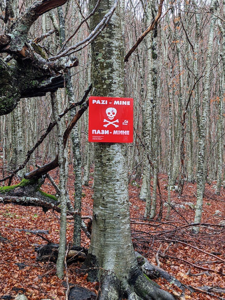 a sign along a hiking trail in bosnia and herzegovina warning of mines.