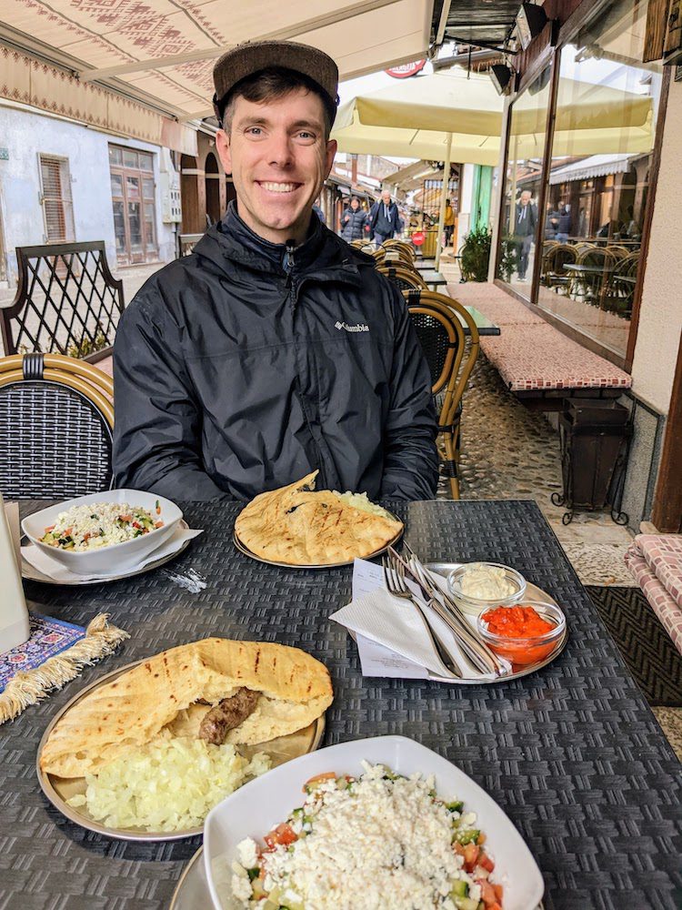 man getting ready to dive into the Balkan favorite: ćevapi. Grilled sausage, onions, jogurt, and pita.