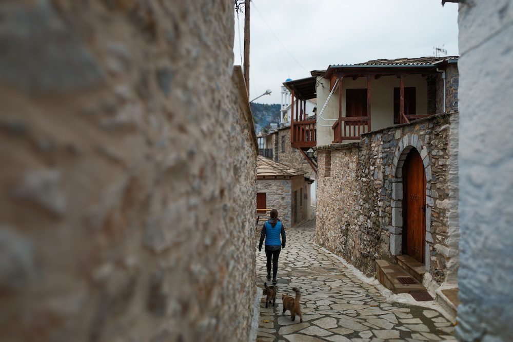 Rose being followed by two of the neighbors through the tight, winding streets of Kastanitsa